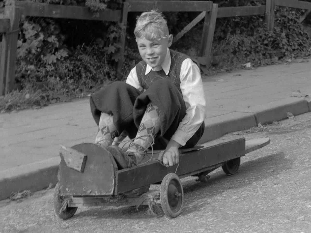 A boy riding a homemade soap box cart: a plank on four small wheels, with a string running forward
to the pivoting front axle
